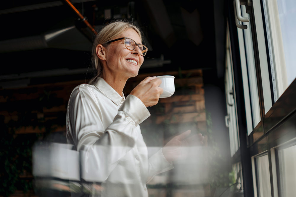 Kvinna som dricker kaffe och ser glad ut.